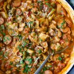 Cabbage Sausage White Bean Skillet in a white enamel cast iron pan with a serving spoon.