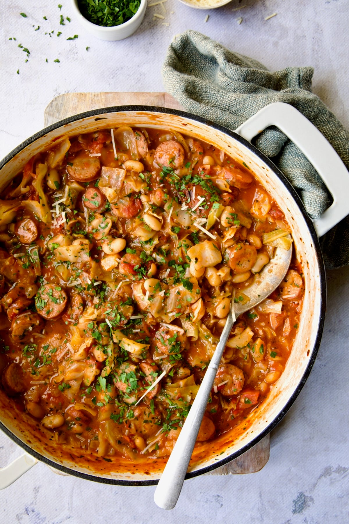 Cabbage Sausage White Bean Skillet in a white enamel cast iron pan with a serving spoon.