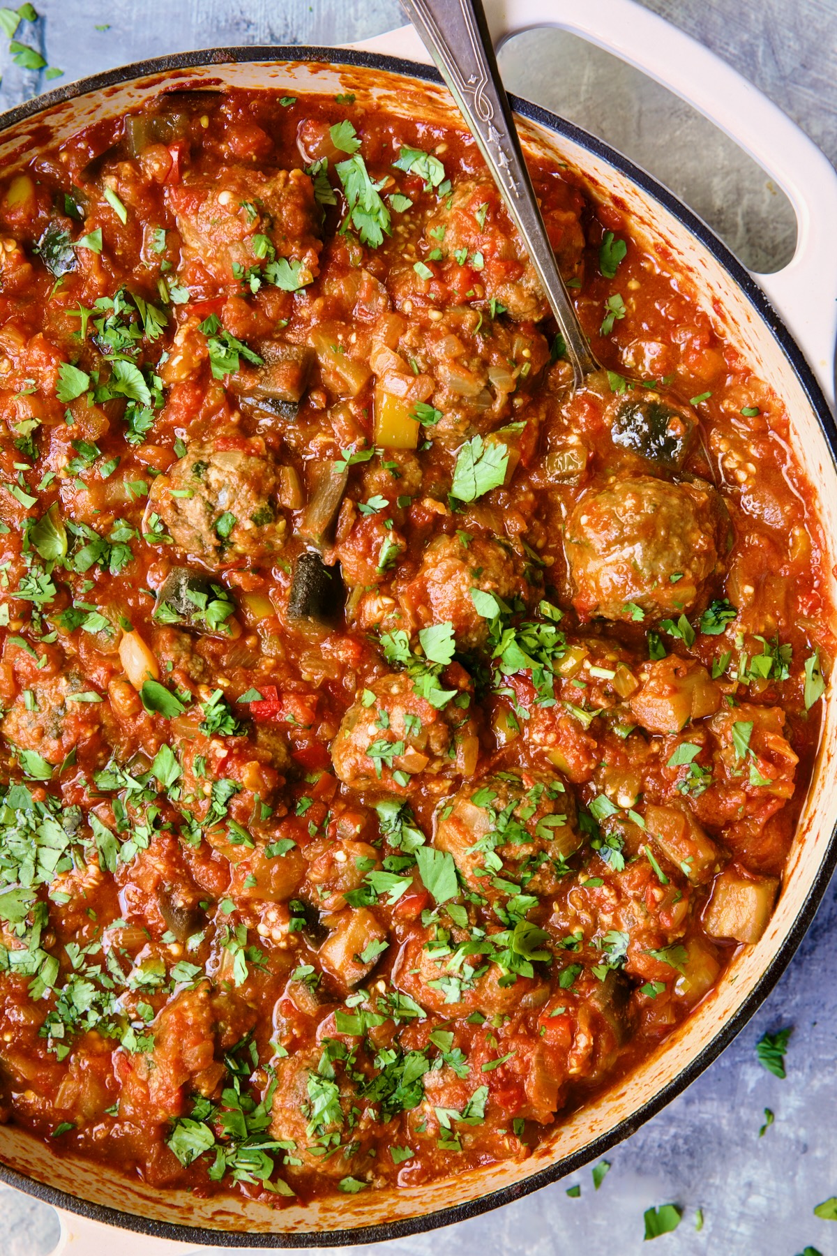 Moroccan Meatball Stew in white enamel cast iron skillet with serving spoon.