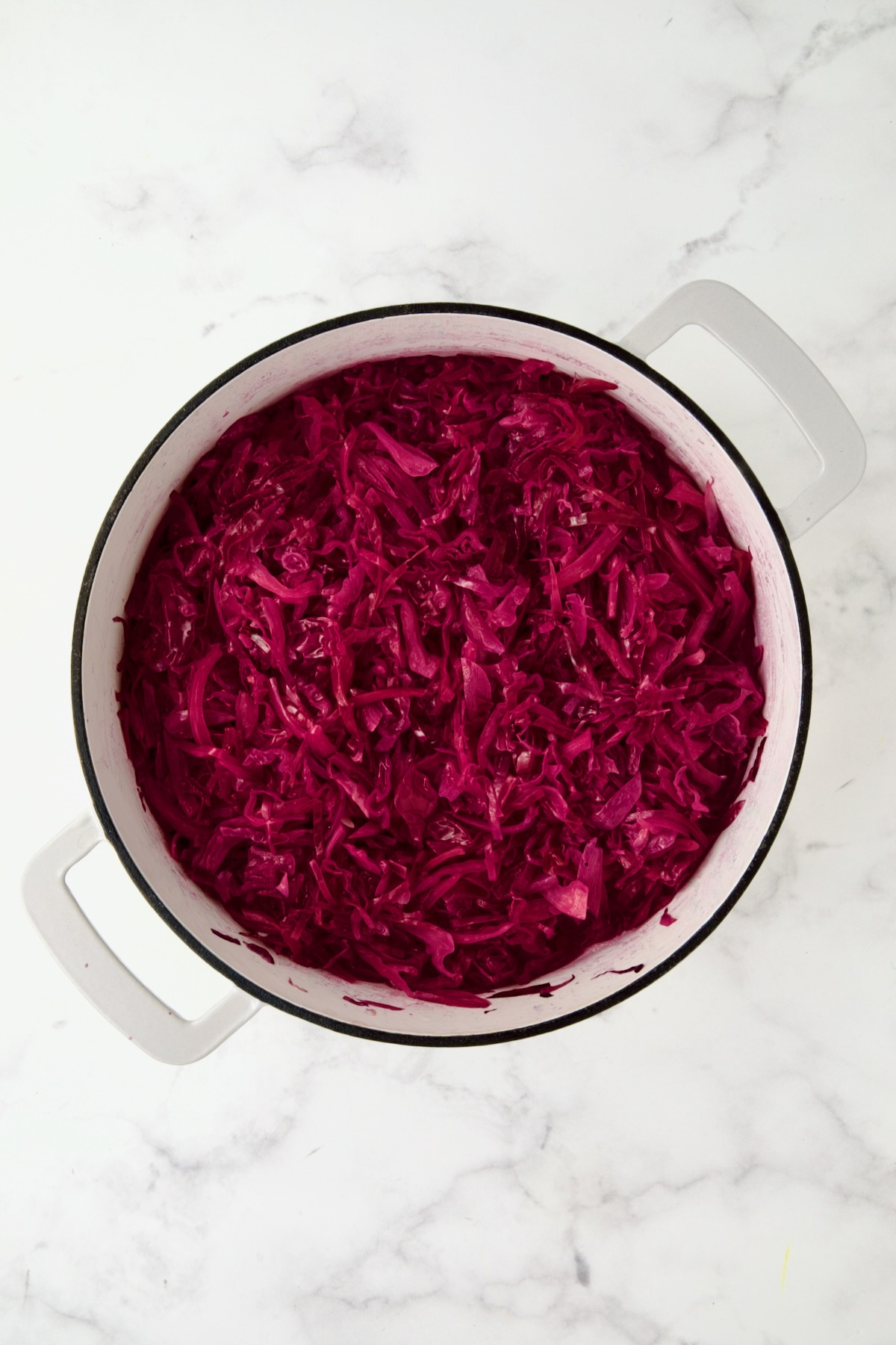 Partially cooked red cabbage in white enamel cast iron skillet.