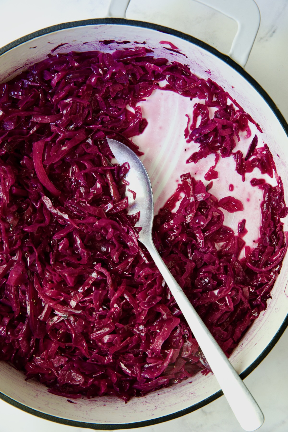 Fully cooked red cabbage in white enamel cast iron skillet with serving spoon.