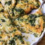 Crustless Spinach Artichoke Quiche in white quiche pan with server lifting one out.
