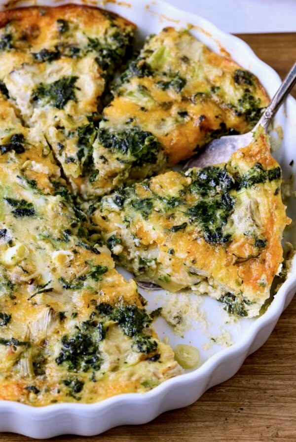 Crustless Spinach Artichoke Quiche in white quiche pan with server lifting one out.