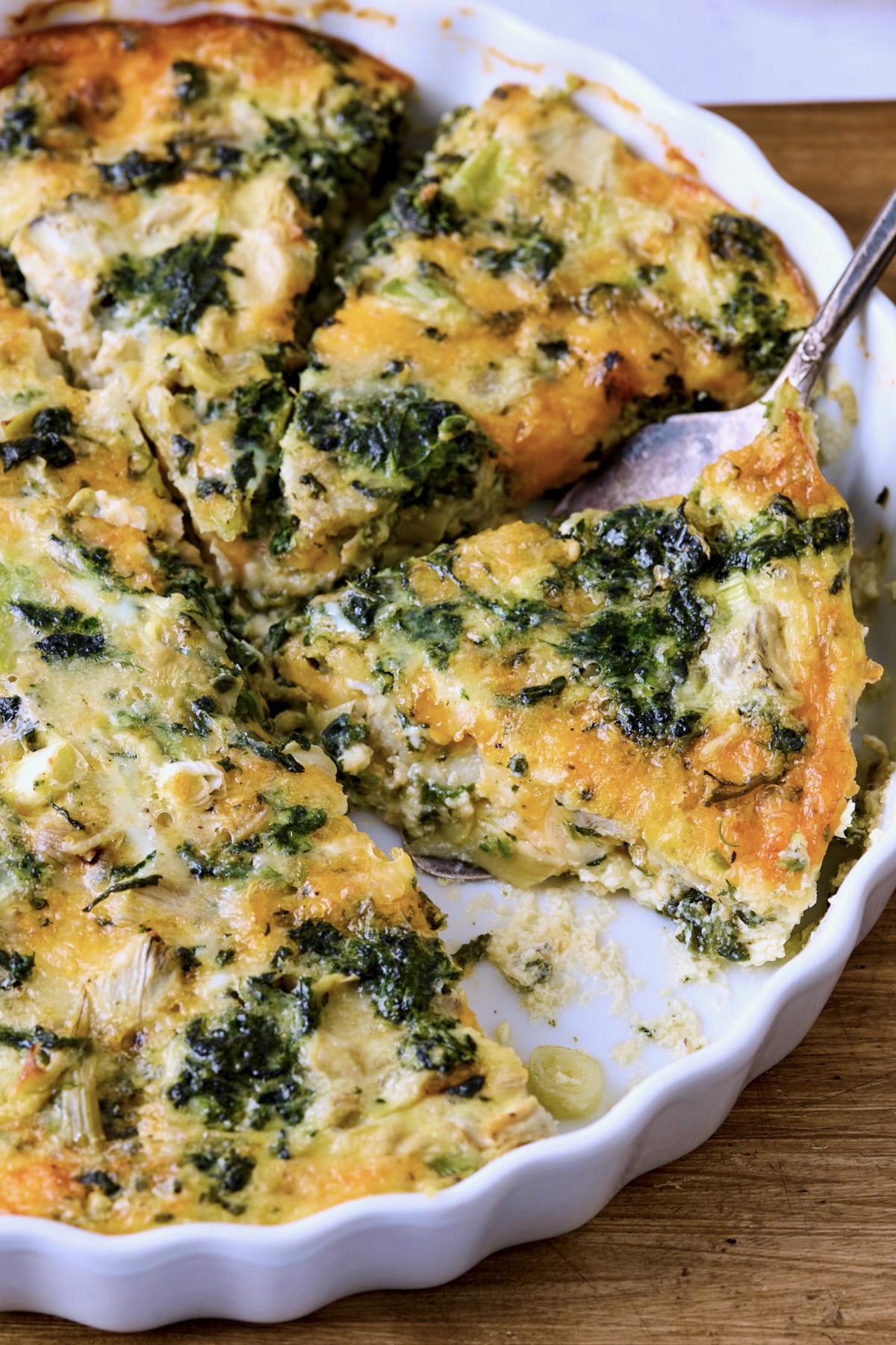 Crustless Spinach Artichoke Quiche in white quiche pan with server lifting one out.