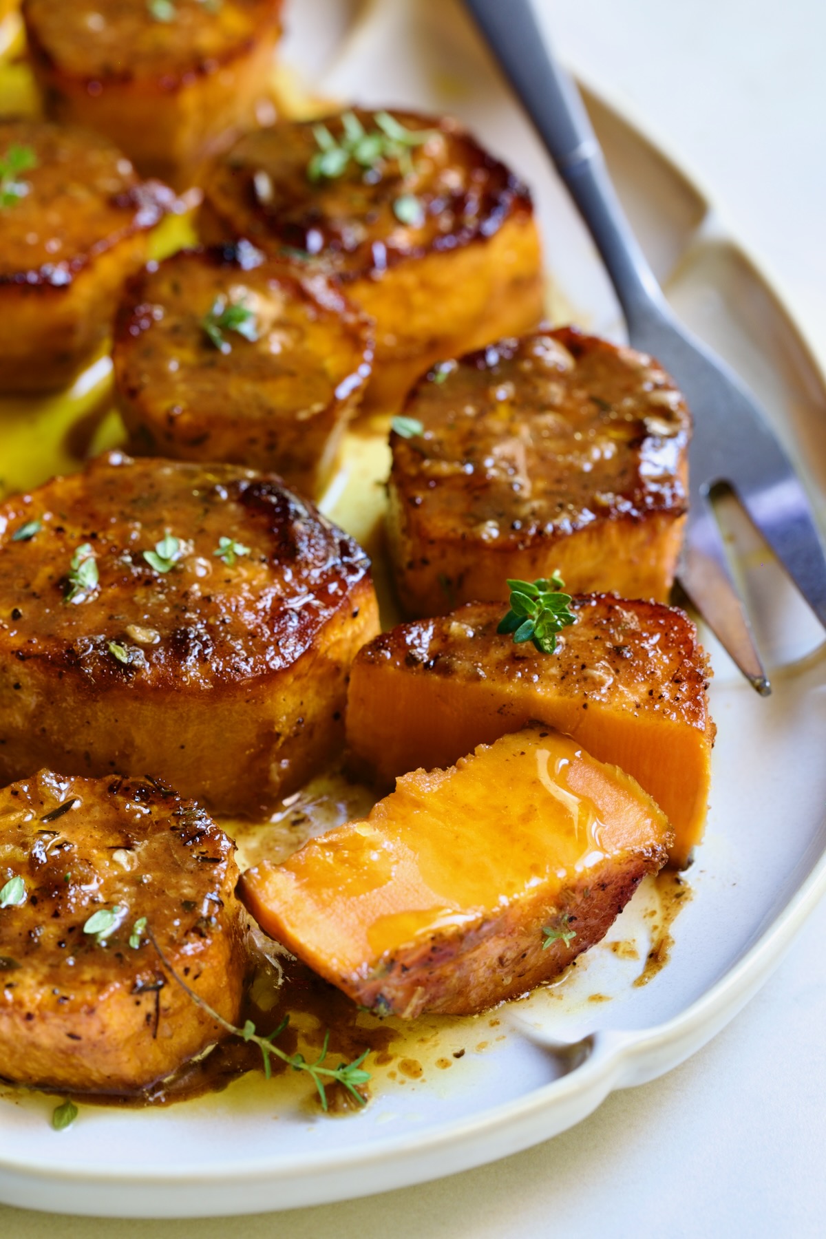 Fondant Sweet Potatoes garnished with fresh thyme on white oval platter with one cut in half.