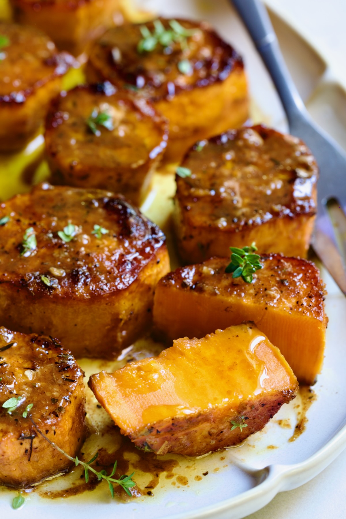 Fondant Sweet Potatoes garnished with fresh thyme on white oval platter with one cut in half.