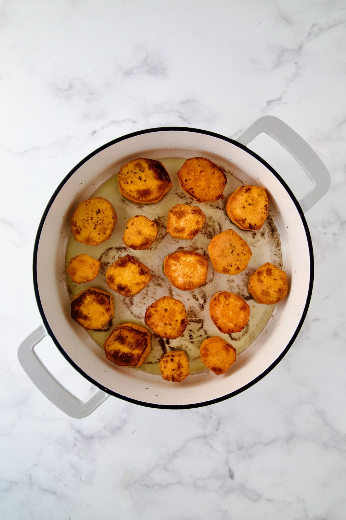 Rounds of sweet potatoes in white enamel cast iron skillet after being browned.