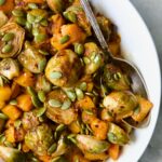 Maple Chili Crisp Brussels Sprouts and Butternut Squash garnished with pepitas in white bowl with serving spoon.