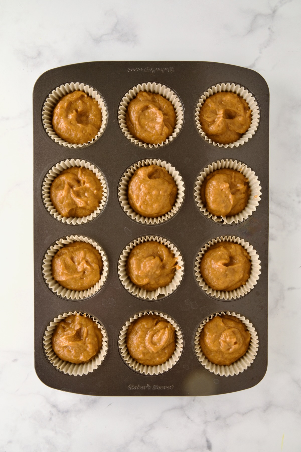 Batter for muffins in a 12-cup muffin pan before the streusel is added.