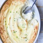 Twice-Baked Mashed Potatoes in white oval baking dish with serving spoon scooping some out.