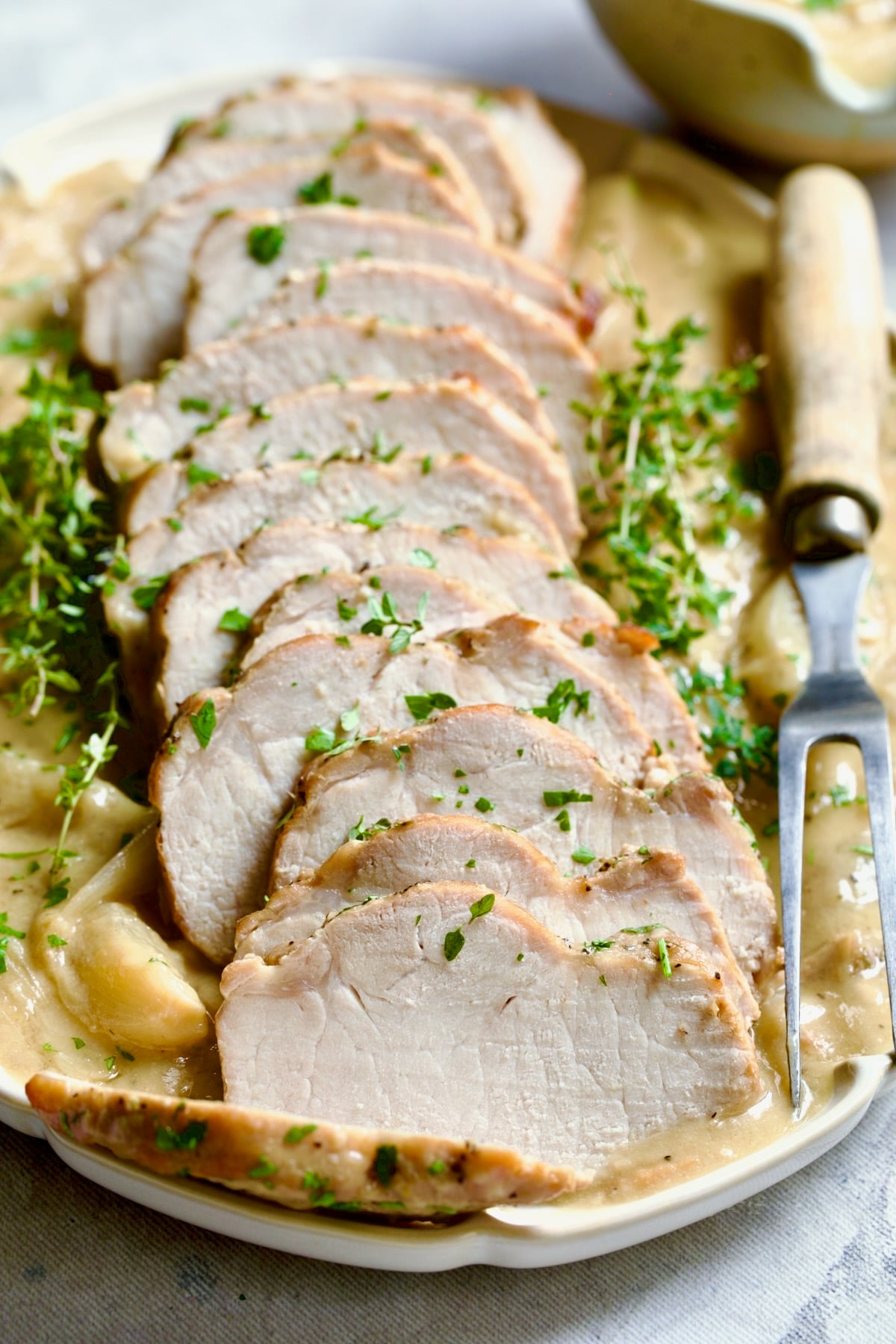 Braised Pork Loin in Dijon Mustard Sauce on a scalloped oval platter with meat fork garnished with thyme sprigs.