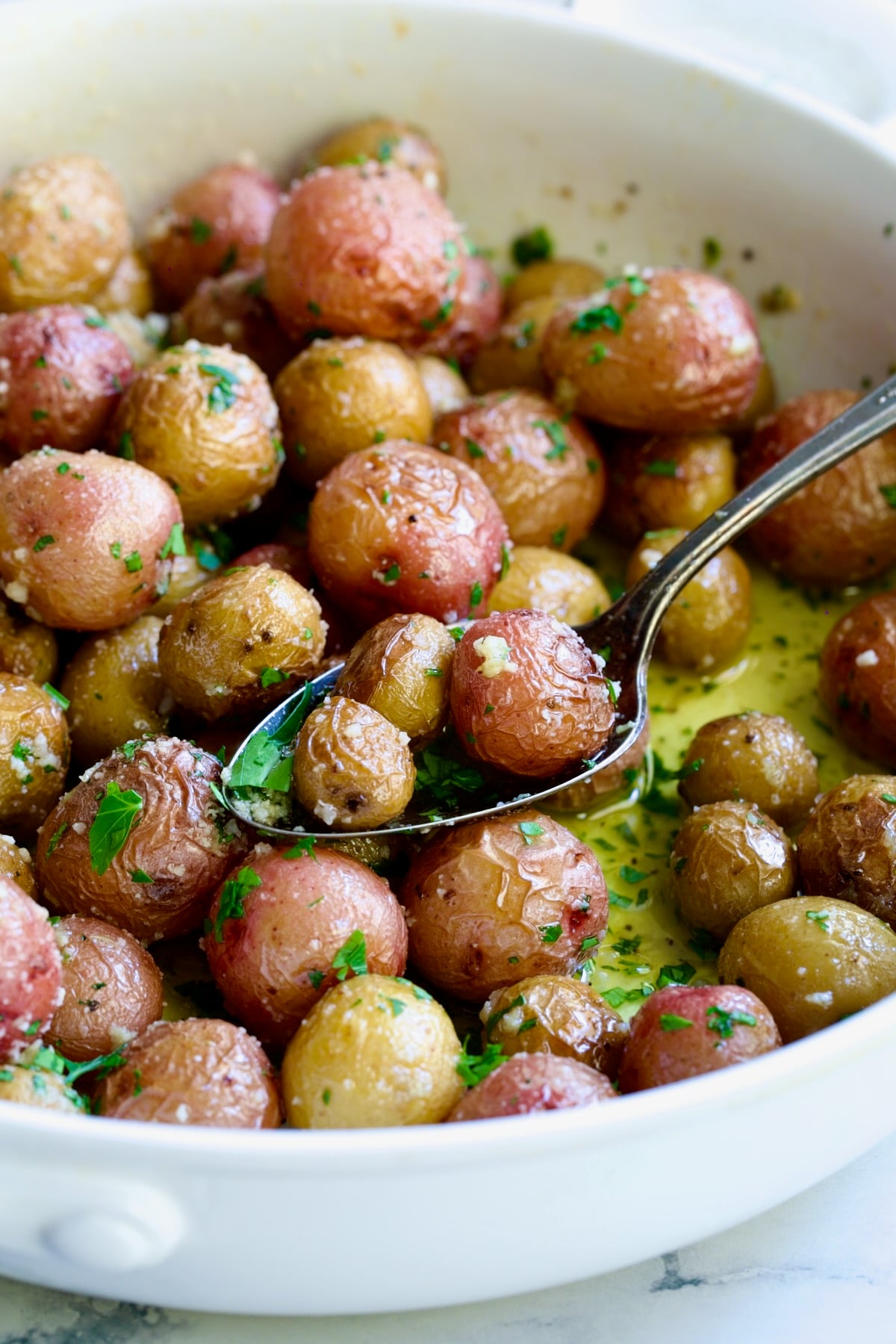 Garlic Butter Parmesan Mini Potatoes in round white baking dish with three on a serving spoon.