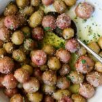 Garlic Butter Parmesan Mini Potatoes in round white baking dish with serving spoon.