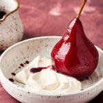 Poached pear sliced in half in bowl with Mascarpone Whipped Cream.