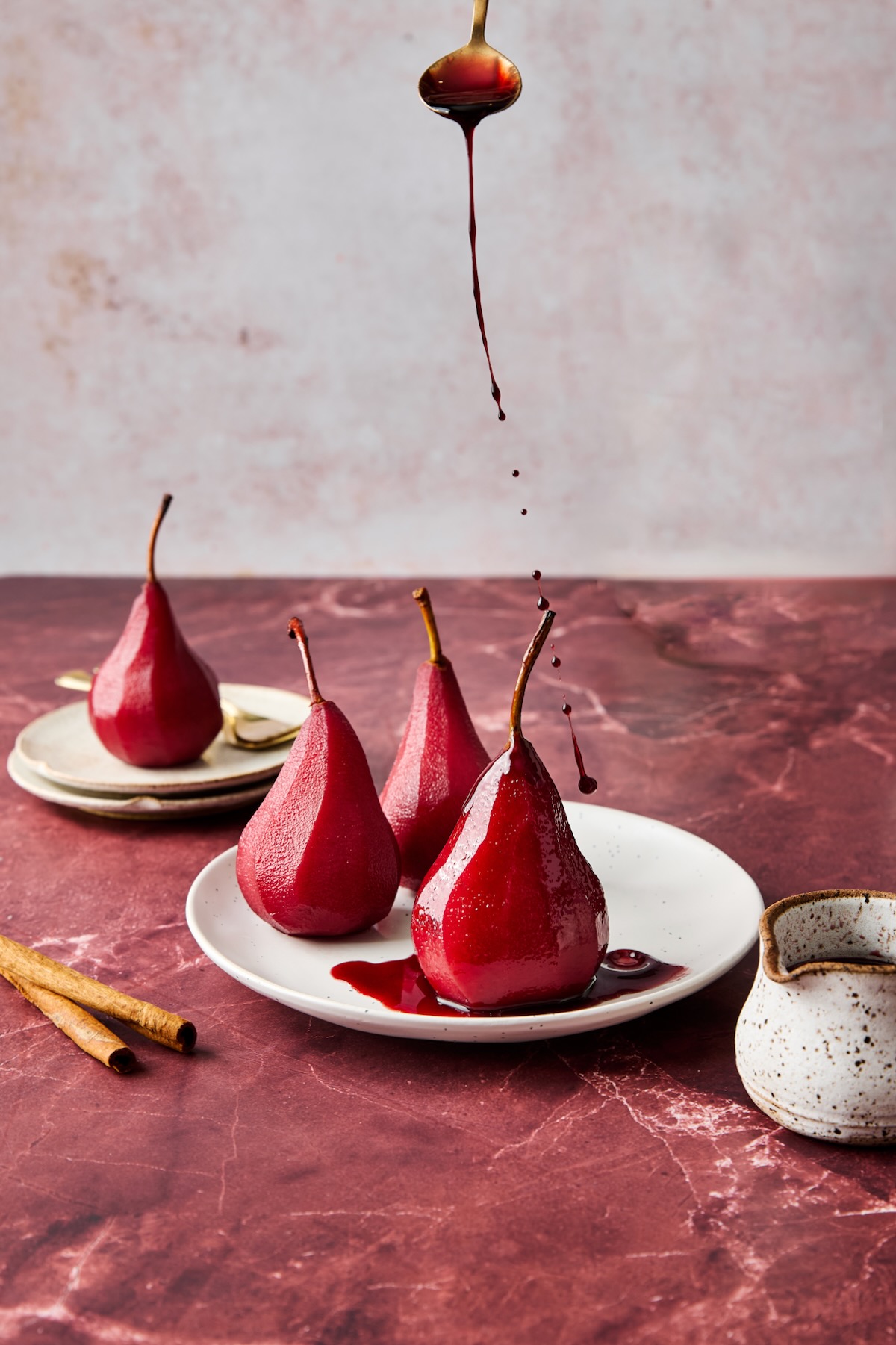 Three poached pears on white plate being drizzled with sauce.