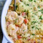 Shrimp and Grits Casserole in oval white baking dish with serving spoon.