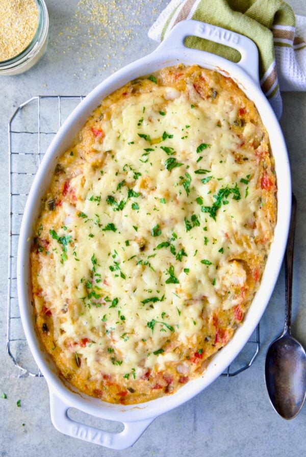 Shrimp and Grits Casserole in oval white baking dish with serving spoon.
