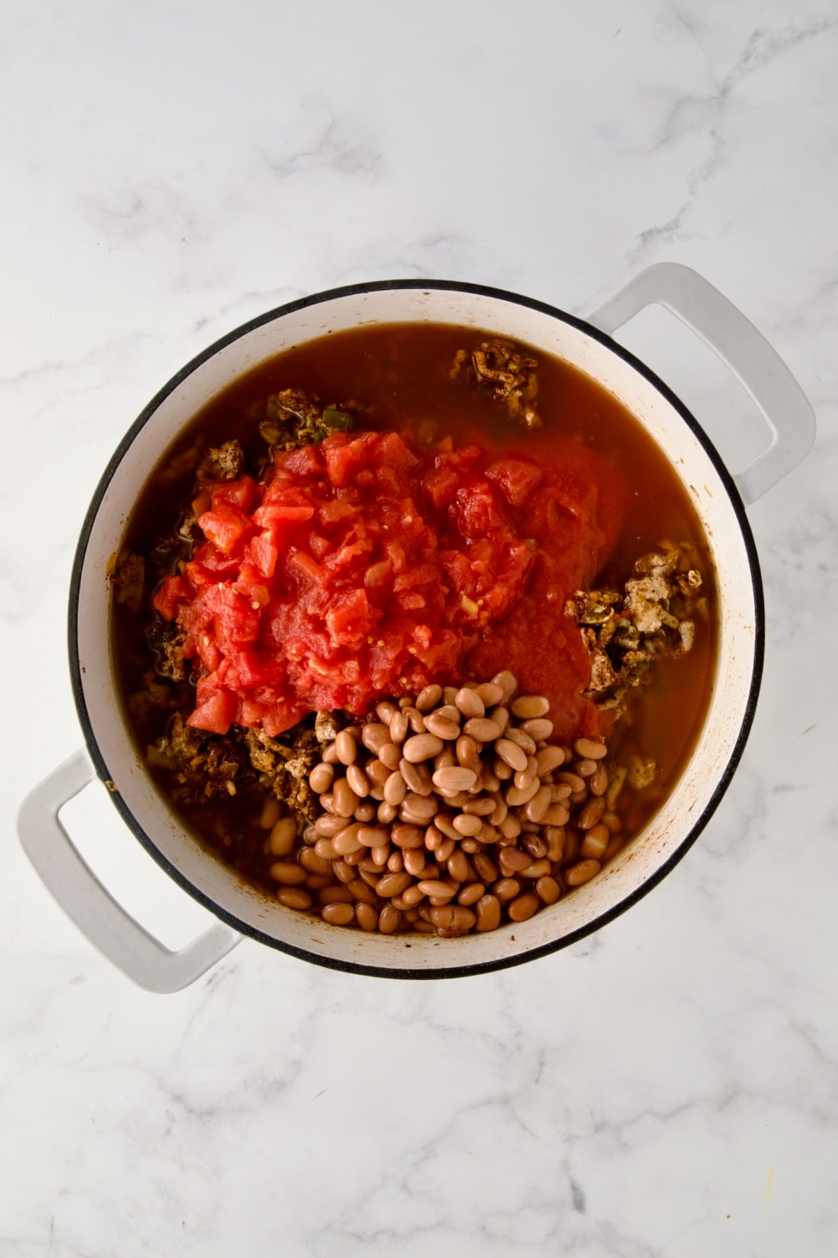 Diced tomatoes, tomato sauce, beans and broth added to ground turkey, onions and green pepper in white enamel cast iron skillet.