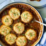 Biscuit-Topped Turkey Skillet Chili in white enamel cast iron skillet with a piece removed onto a small plate.