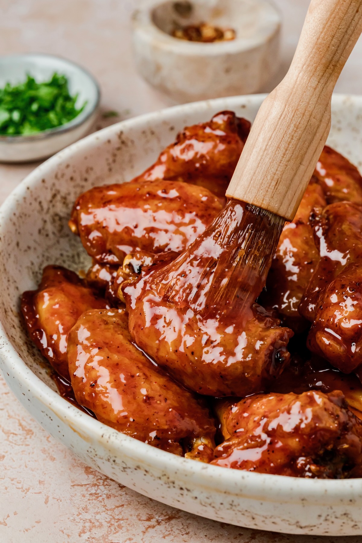 Hot Honey Chicken Wings in speckled bowl being brushed with glass with basting brush.