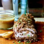Pecan-Crusted Pork Tenderloin with Bourbon - Mustard Sauce on wood cutting board.