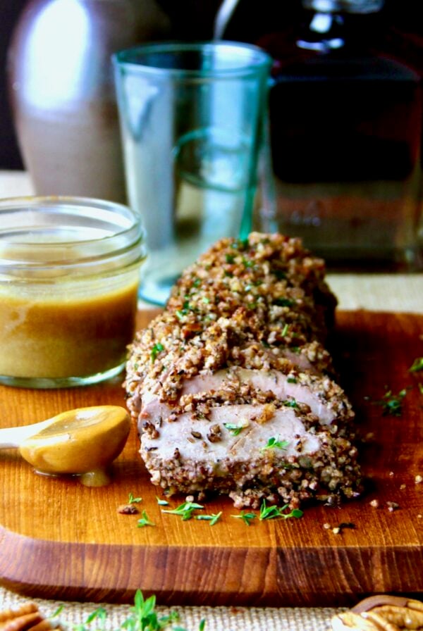 Pecan-Crusted Pork Tenderloin with Bourbon - Mustard Sauce on wood cutting board.