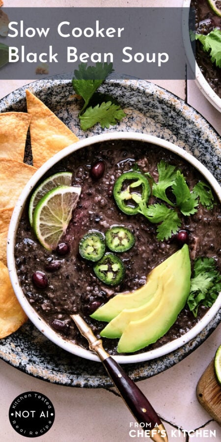 Pinterest graphic for Slow Cooker Black Bean Soup showing it in a white bowl garnished with lime wedges, jalapeno slices, cilantro and avocado.