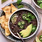 Slow Cooker Black Bean Soup on speckled plate with tortilla chips.