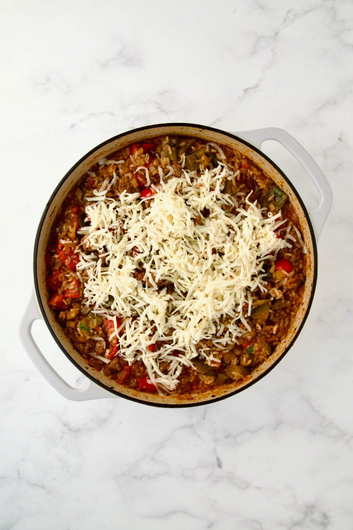 Cheese added to ingredients in white enamel cast iron skillet.