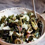 Roasted kale sprouts with shaved Parmesan cheese in white bowl with serving fork.