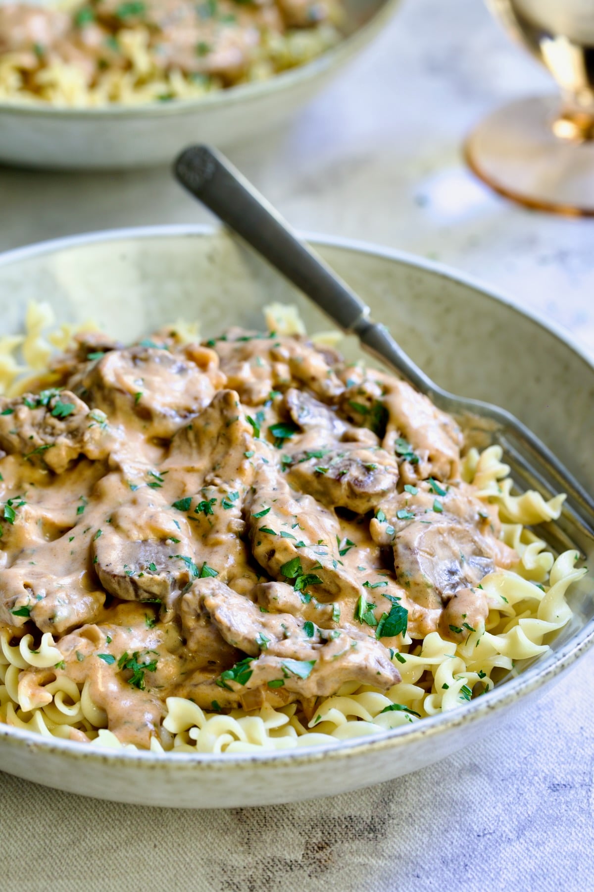 Date Night Beef Stroganoff over curly egg noodles in dinner bowl with fork.