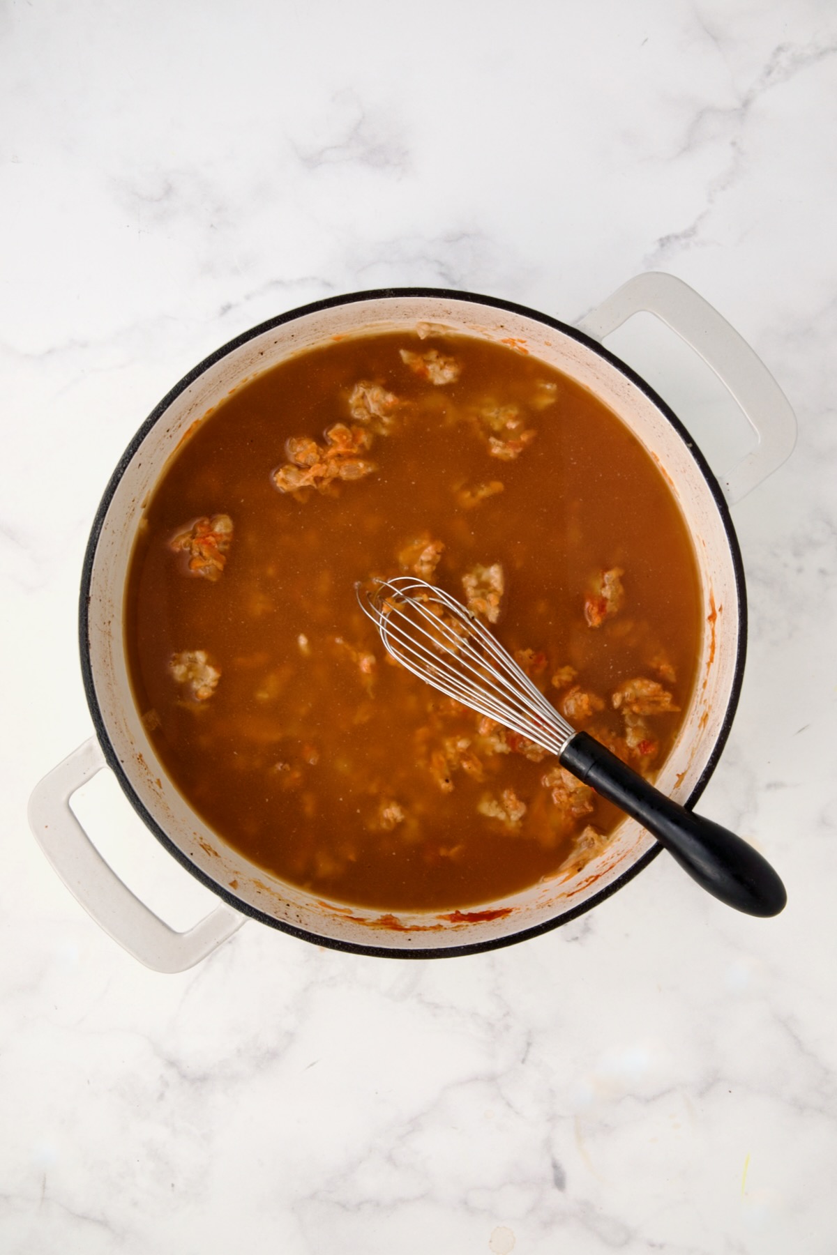 Broth added to tomato paste, wine, onions and flour smoothed out in white enamel cast iron skillet.