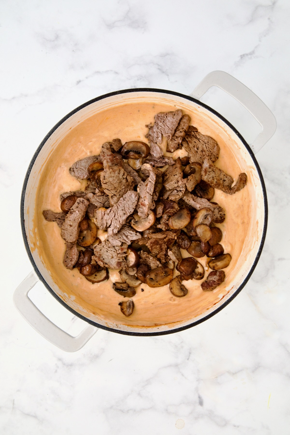 Beef and mushrooms added back to fully thickened sauce in white enamel cast iron skillet.