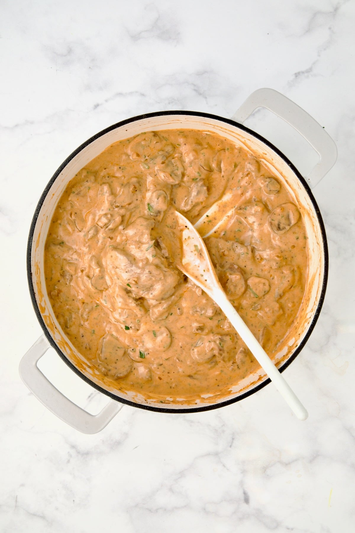 Finished beef stroganoff with white mixing spoon in white enamel cast iron skillet.