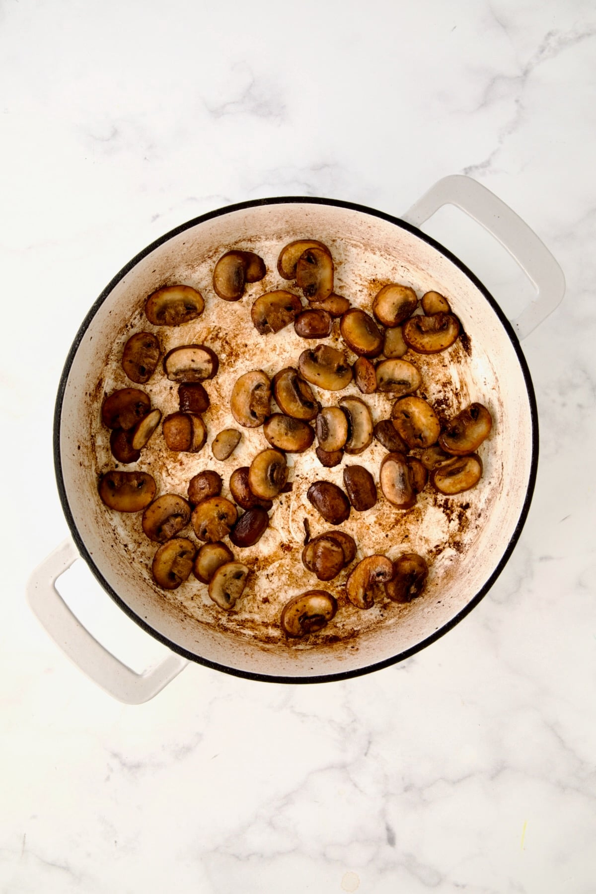 Browned mushrooms in white enamel cast iron skillet.