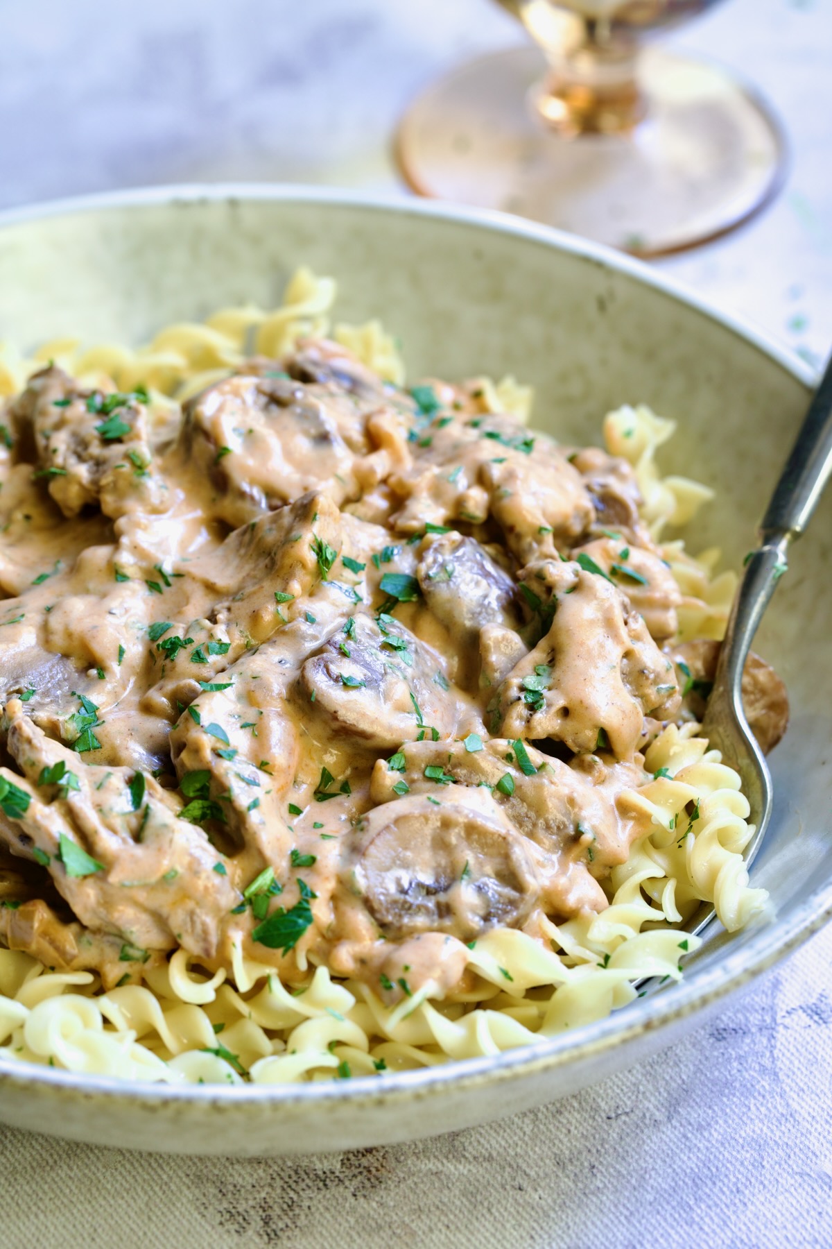 Date Night Beef Stroganoff over curly egg noodles in dinner bowl with dinner fork.