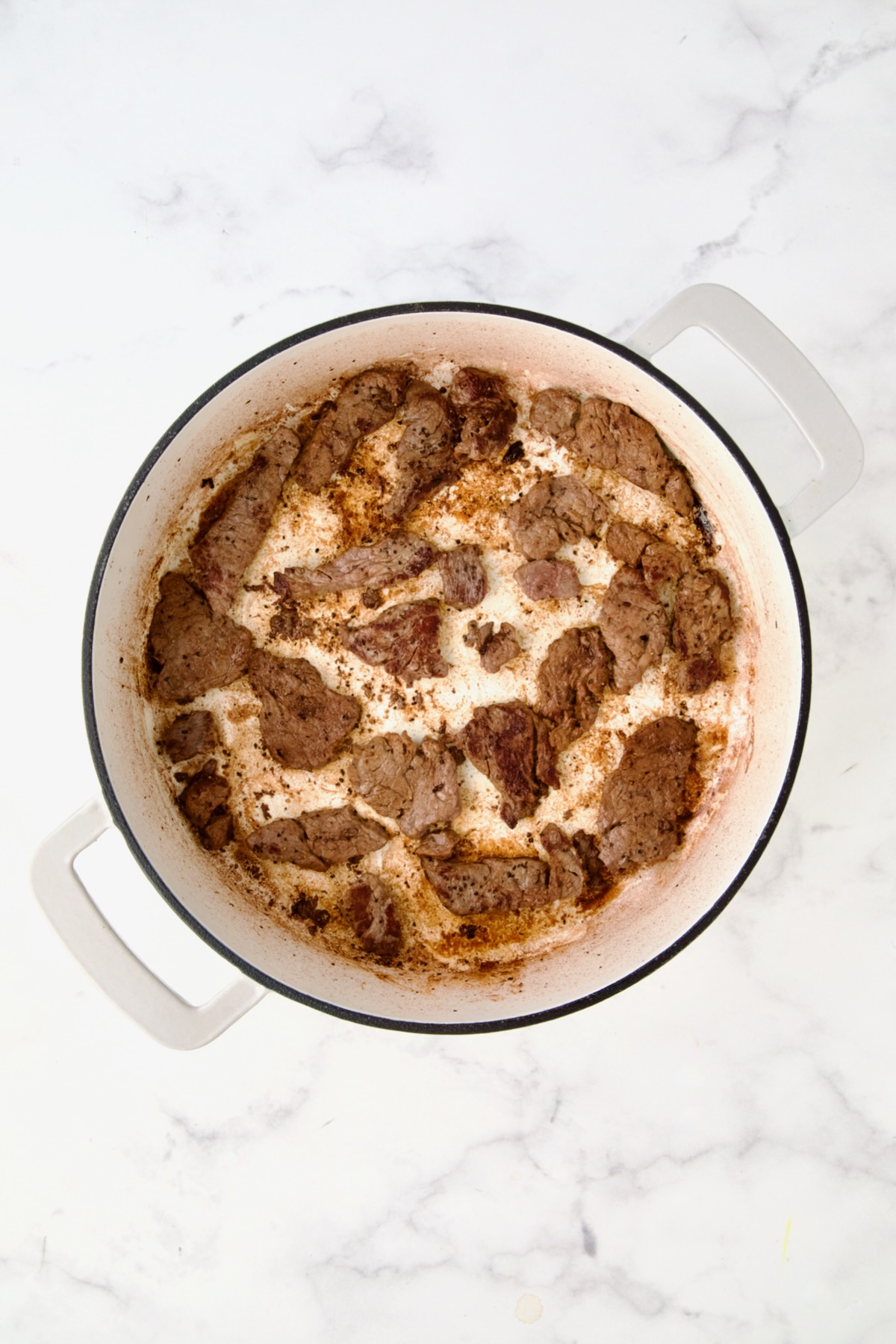 Browned beef tenderloin strips in white enamel casit iron skillet.