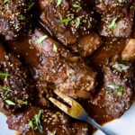 Korean Braised Beef Short Ribs on oval white platter with meat fork sprinkled with sesame seeds and thinly sliced scallions.