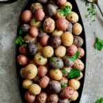 Salt Roasted Baby Potatoes on oval black patter with Sour Cream Horseradish Dip in a black bowl garnished with fresh parsley.
