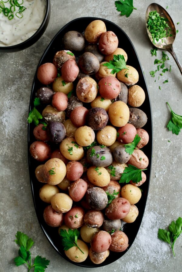 Salt Roasted Baby Potatoes on oval black patter with Sour Cream Horseradish Dip in a black bowl garnished with fresh parsley.