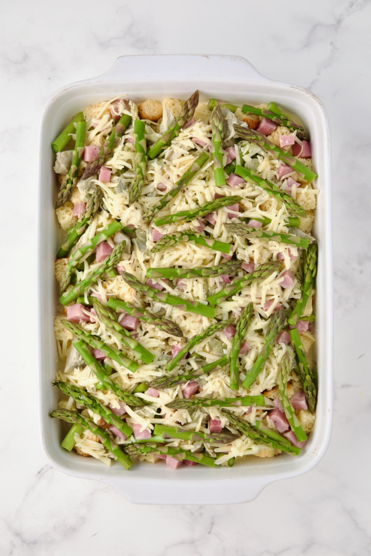 The second layer of bread cubes, ham, asparagus, artichoke hearts completed with top layer of asparagus tips added.
