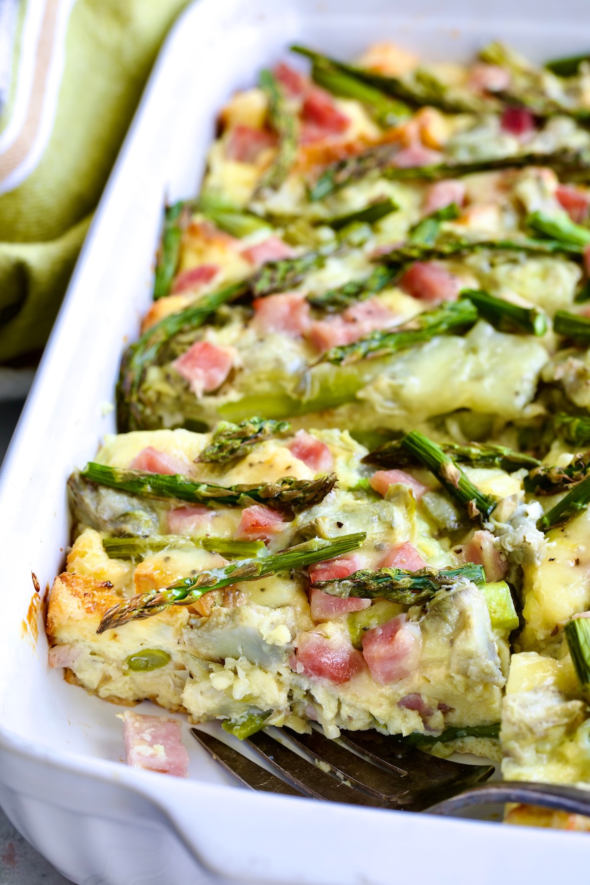 Close-up of a piece of Brioche Breakfast Strata in white rectangular baking dish with serving fork.
