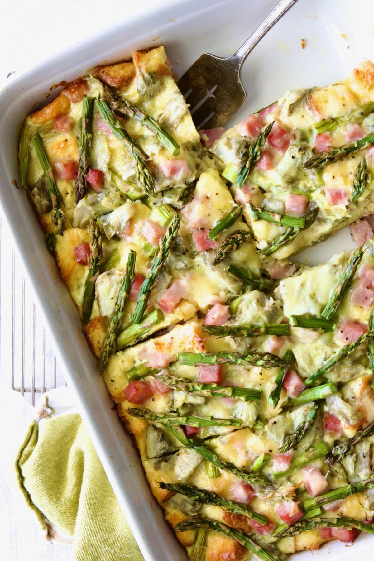 Brioche Breakfast Strata in white rectangular baking dish cut into pieces with one pieces.