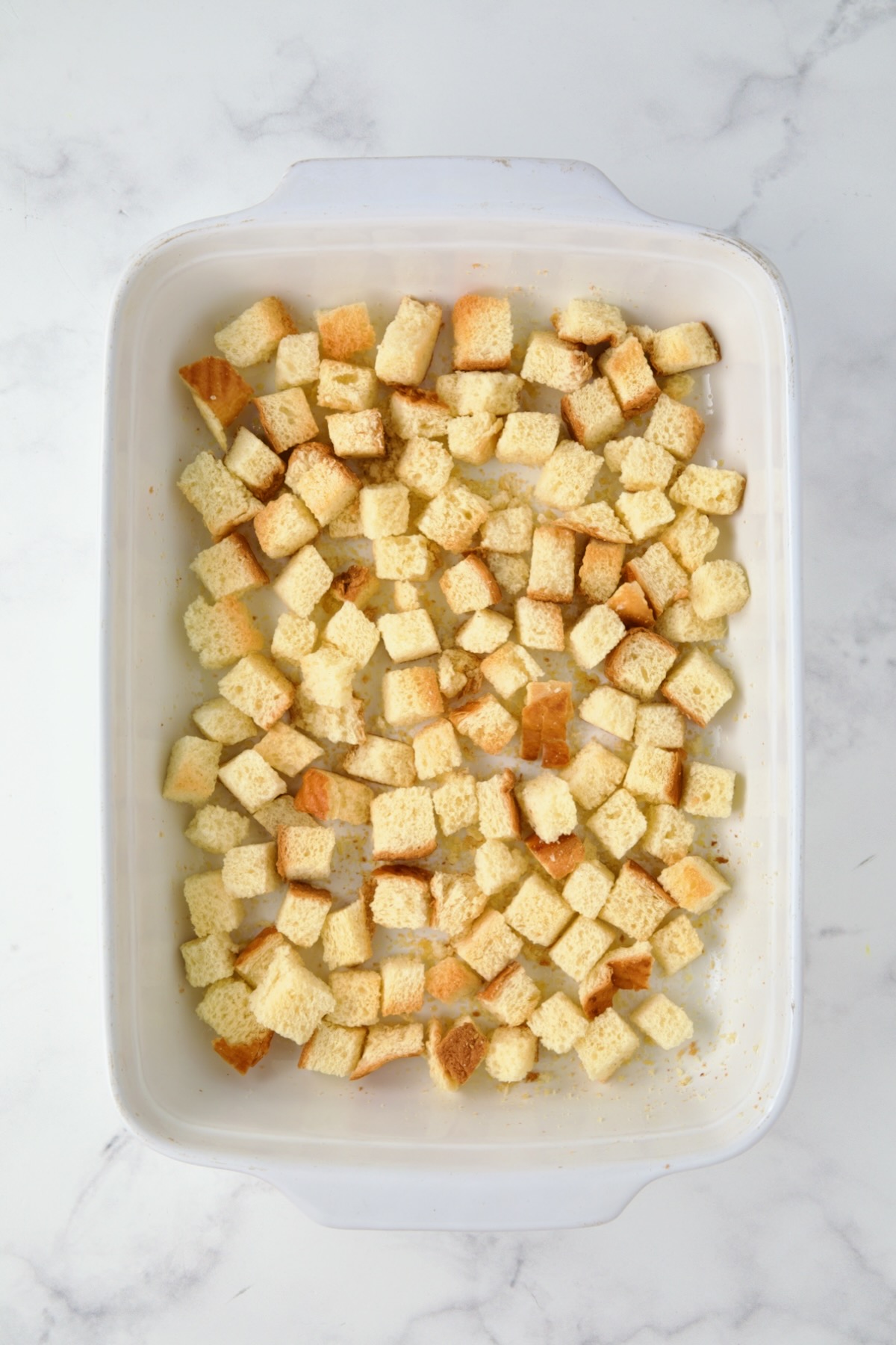 Half of the toasted brioche bread cubes in white rectangular baking dish.
