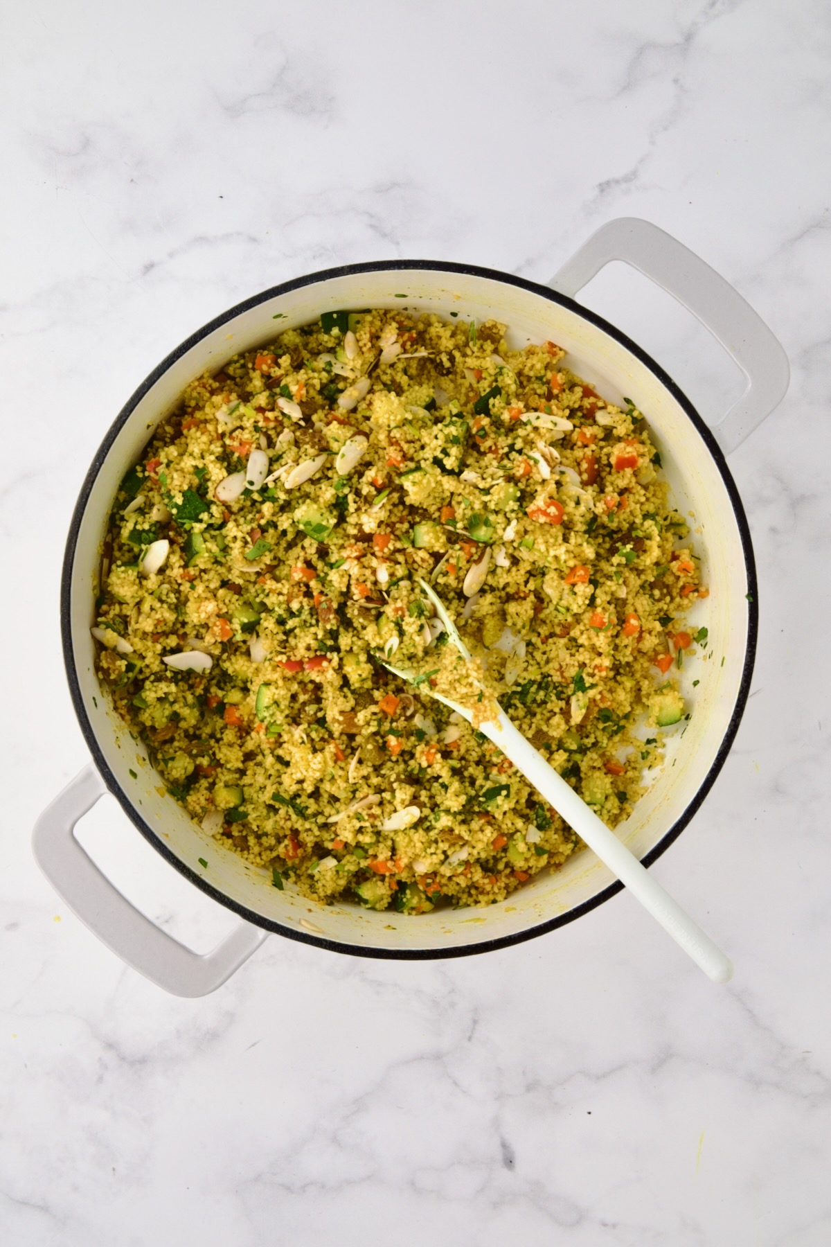 Jeweled Couscous in white enamel cast iron skillet with white mixing spoon.