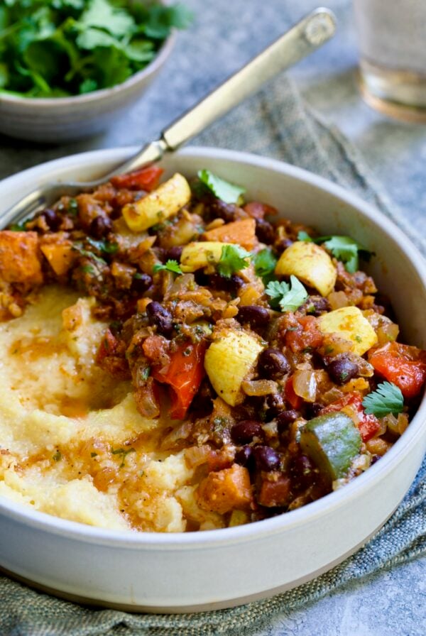 Roasted Vegetable Stew with Polenta in white bowl on blue napkin garnished with fresh cilantro leaves.