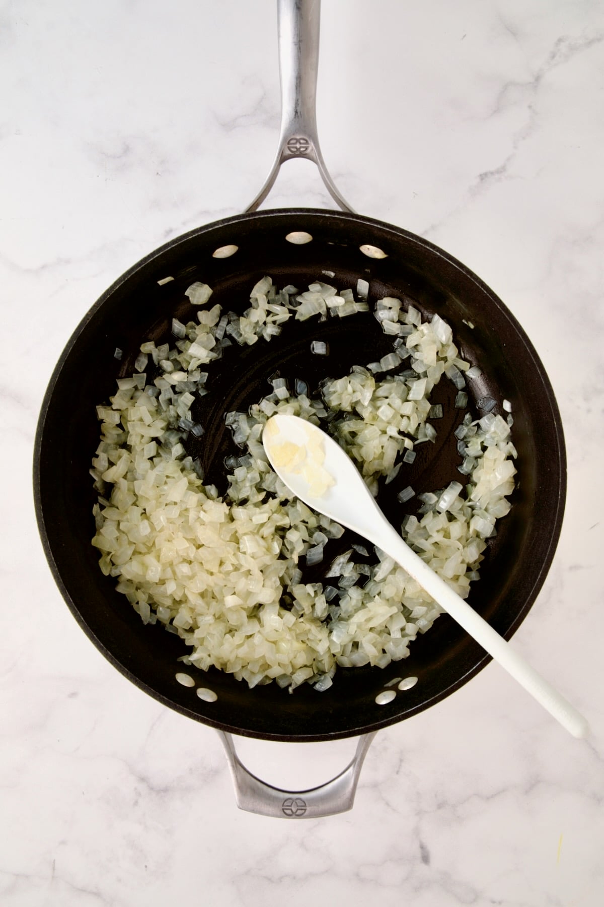 Cooked onions in nonstick skillet being stirred with white spoon.