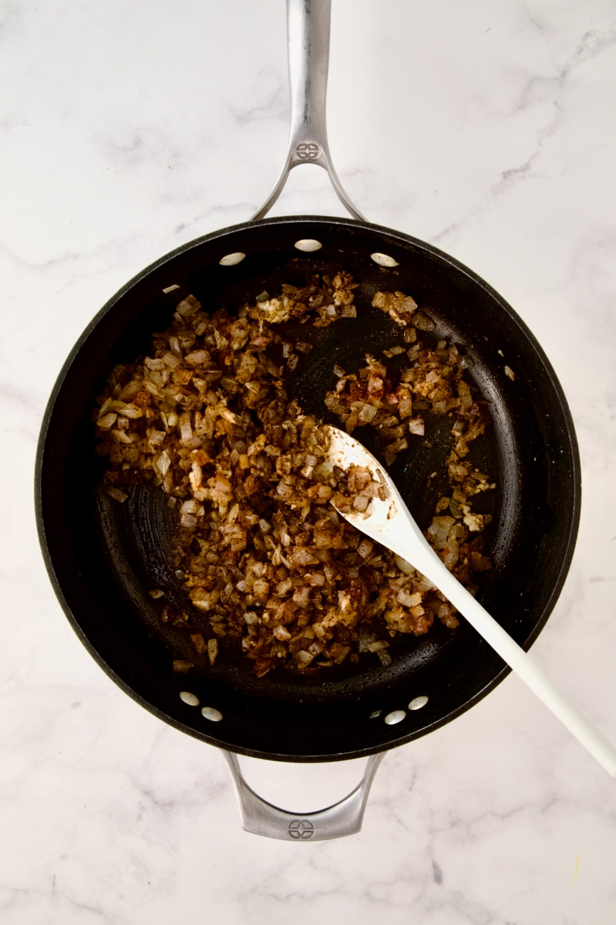 Spices being stirred into cooked onions.