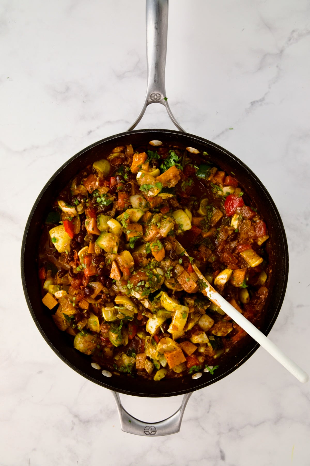 Vegetables being stirred into base in nonstick skillet with white mixing spoon.