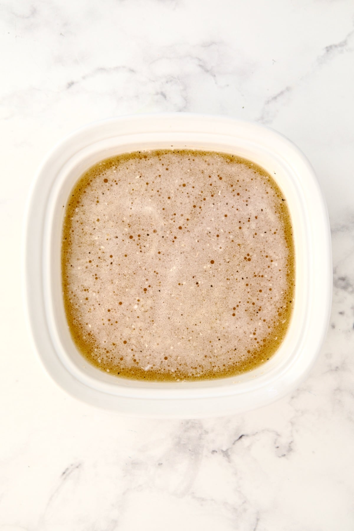 Ingredients for polenta in Corningware baking dish stirred together.